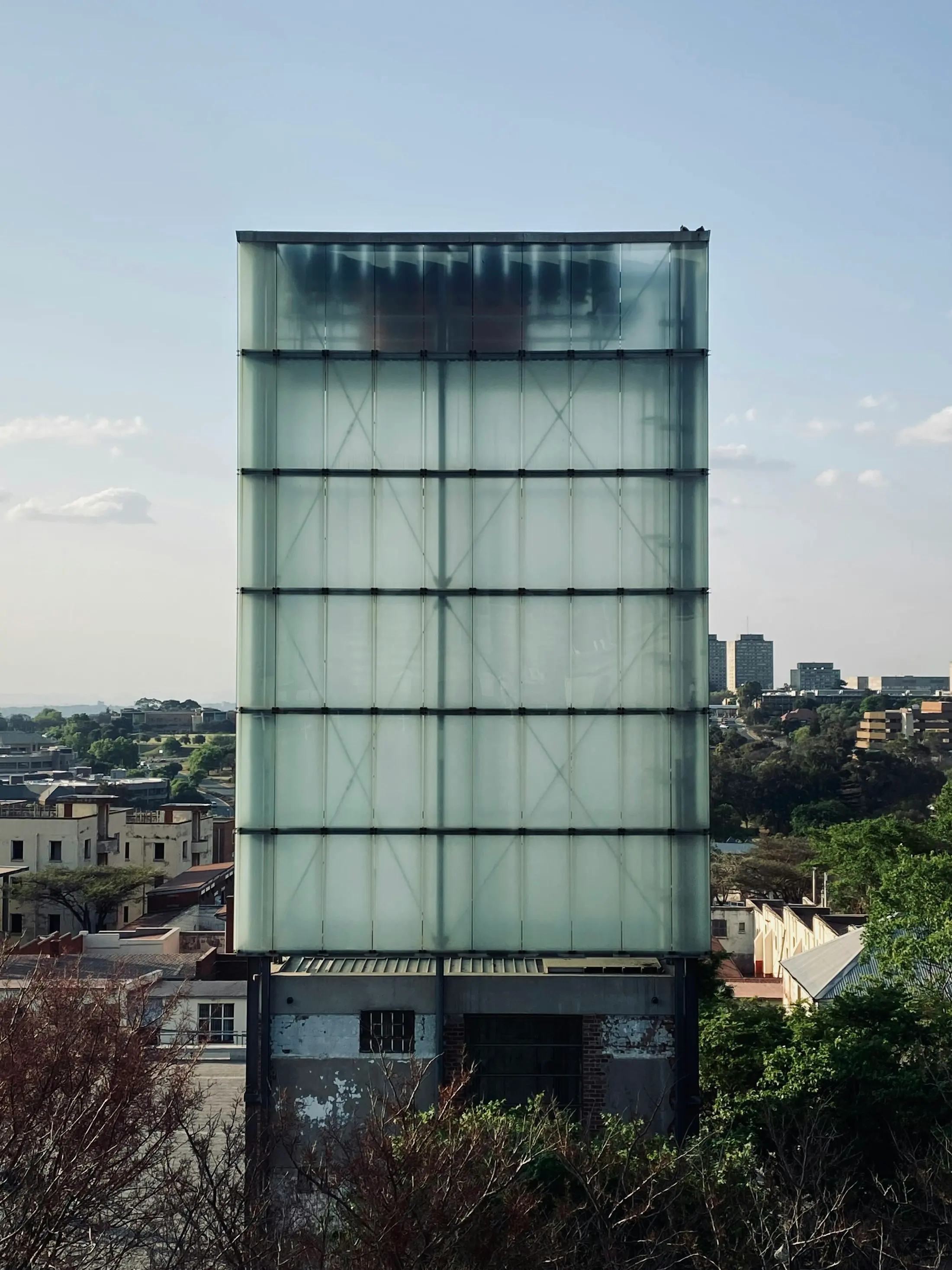 A frosted-glass tower rising above a low-rise city in late-afternoon light