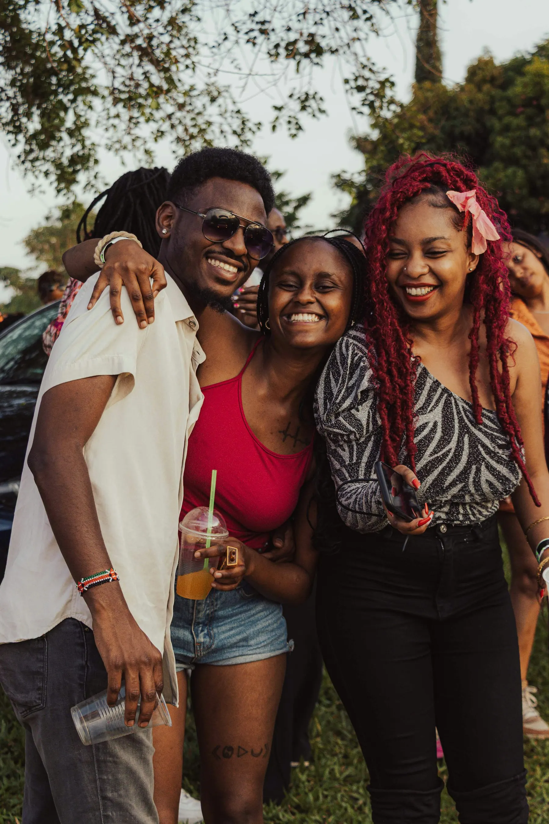 Friends laughing and embracing outdoors among green trees.