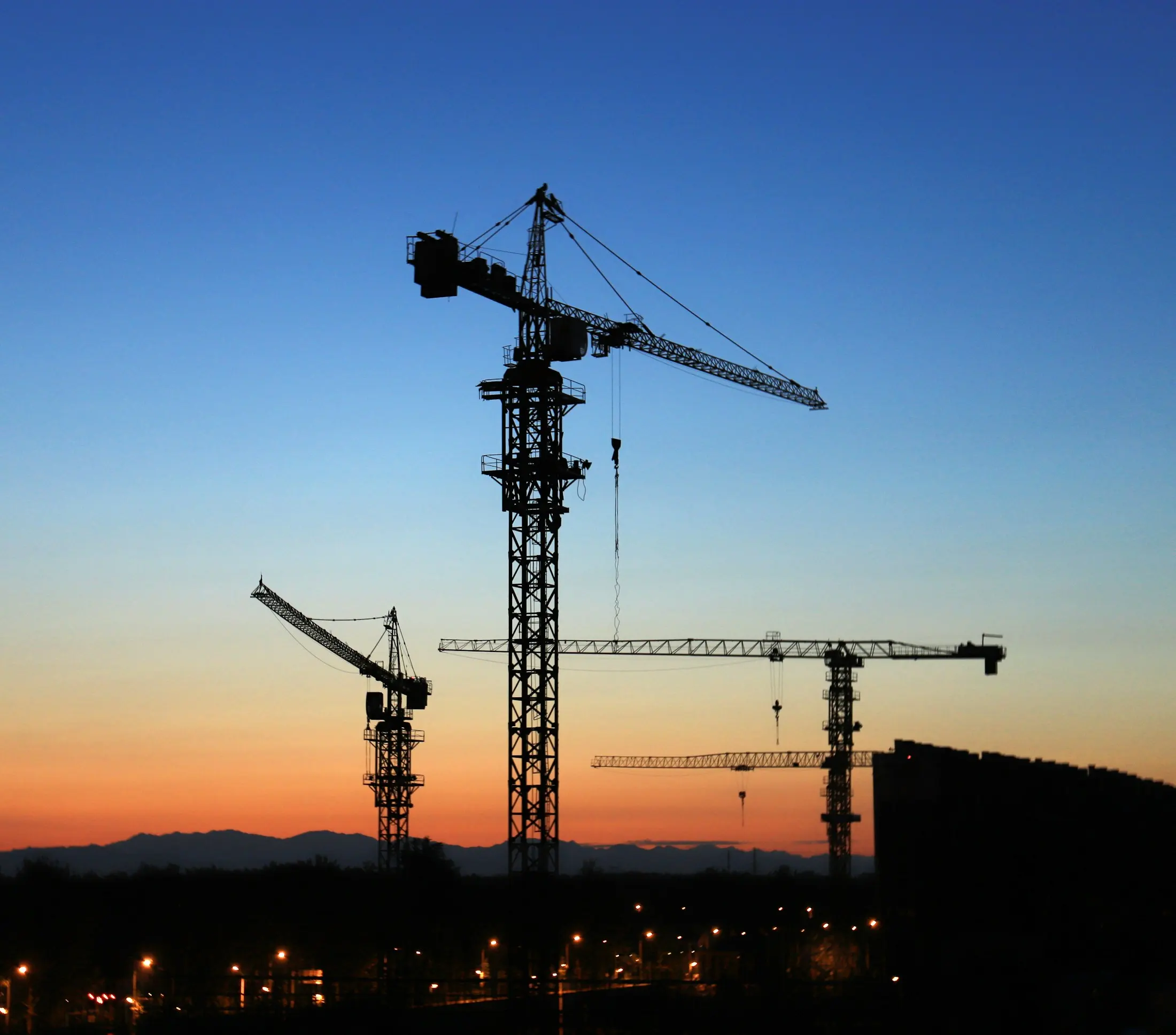 Tower cranes silhouetted against a clear dawn sky over a new building site.