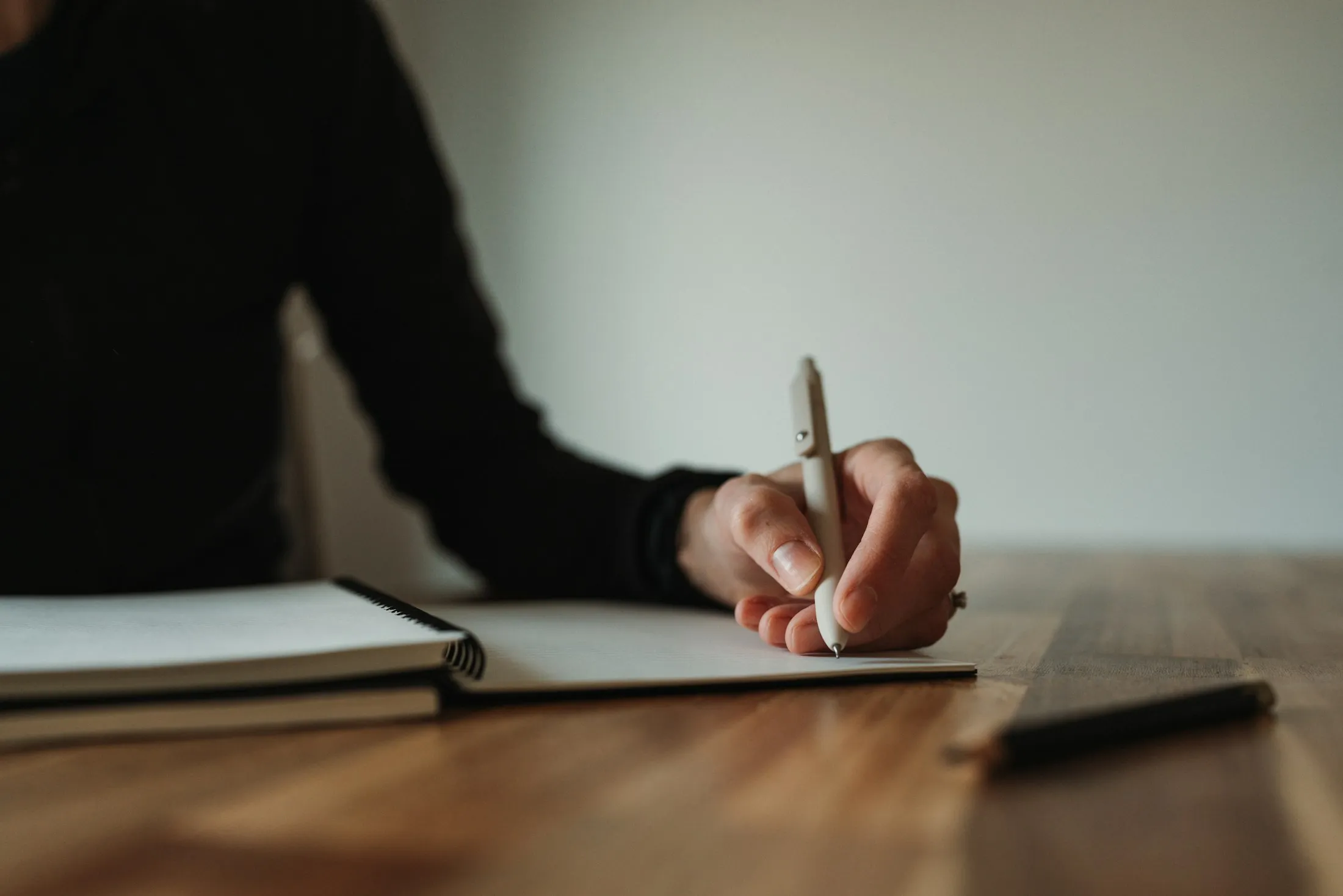 A hand writing in a spiral notebook on a warm wooden table