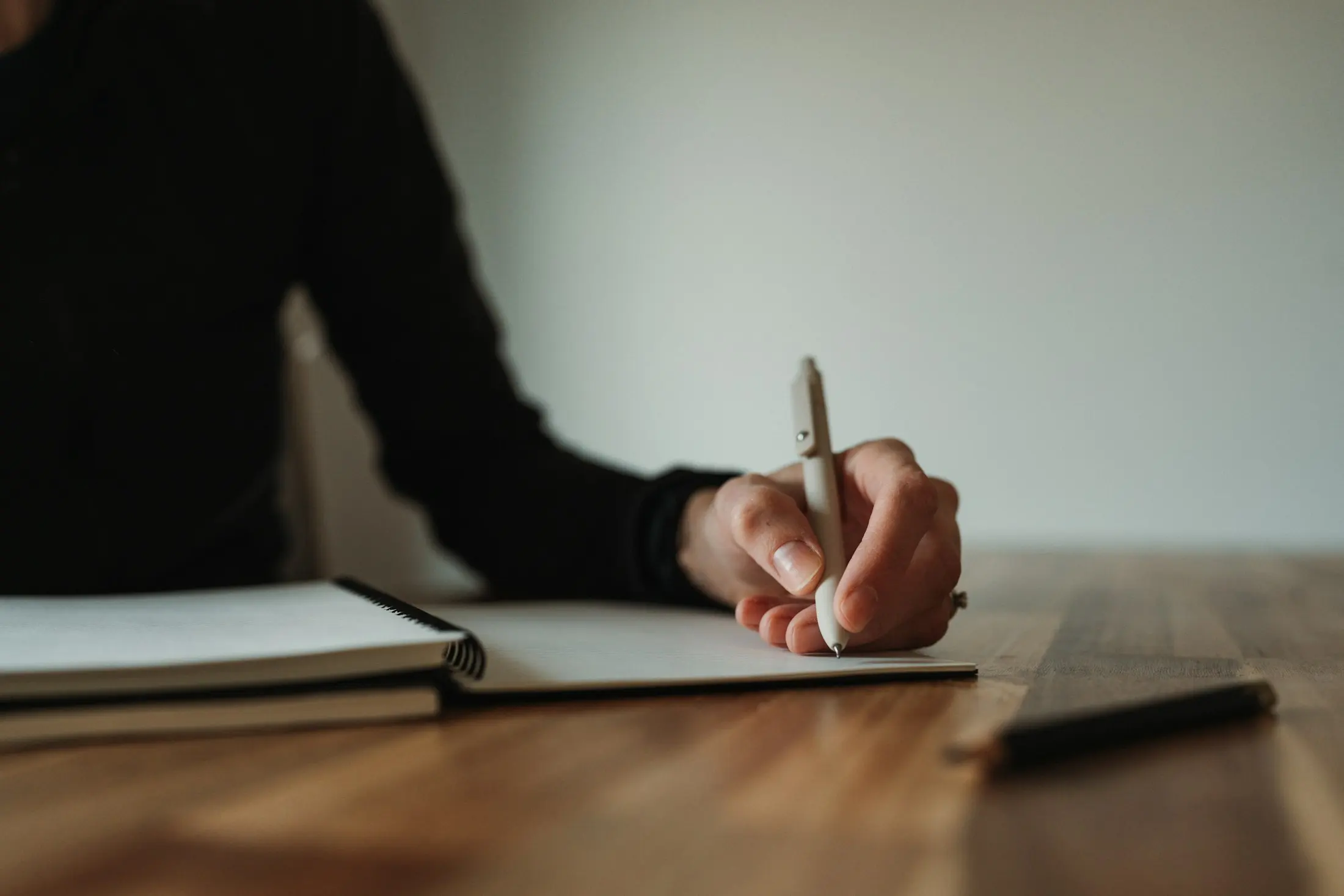 A hand writing in a spiral notebook on a warm wooden table