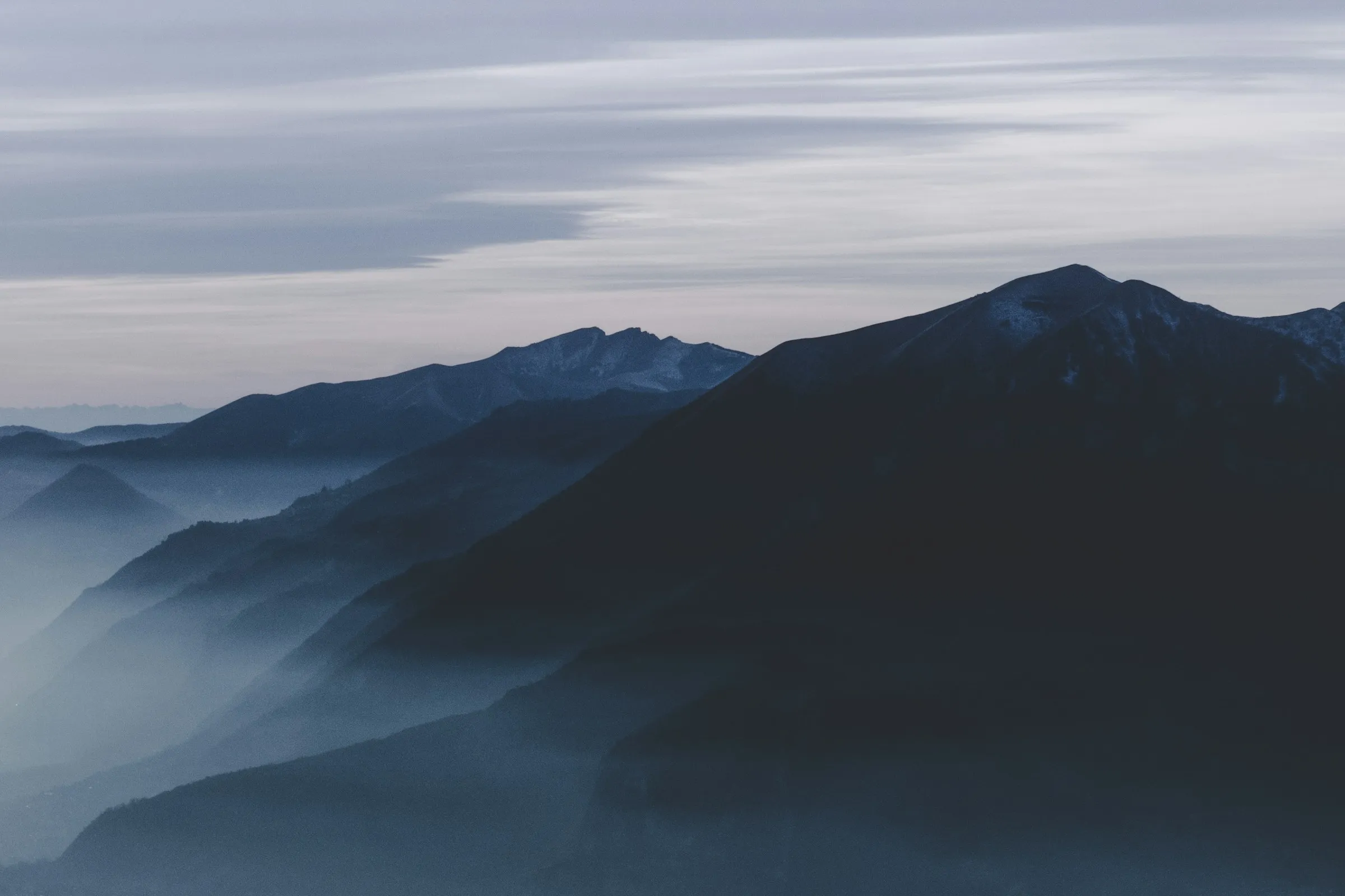 Layered mountain ridges with mist in the valleys under a grey morning sky.