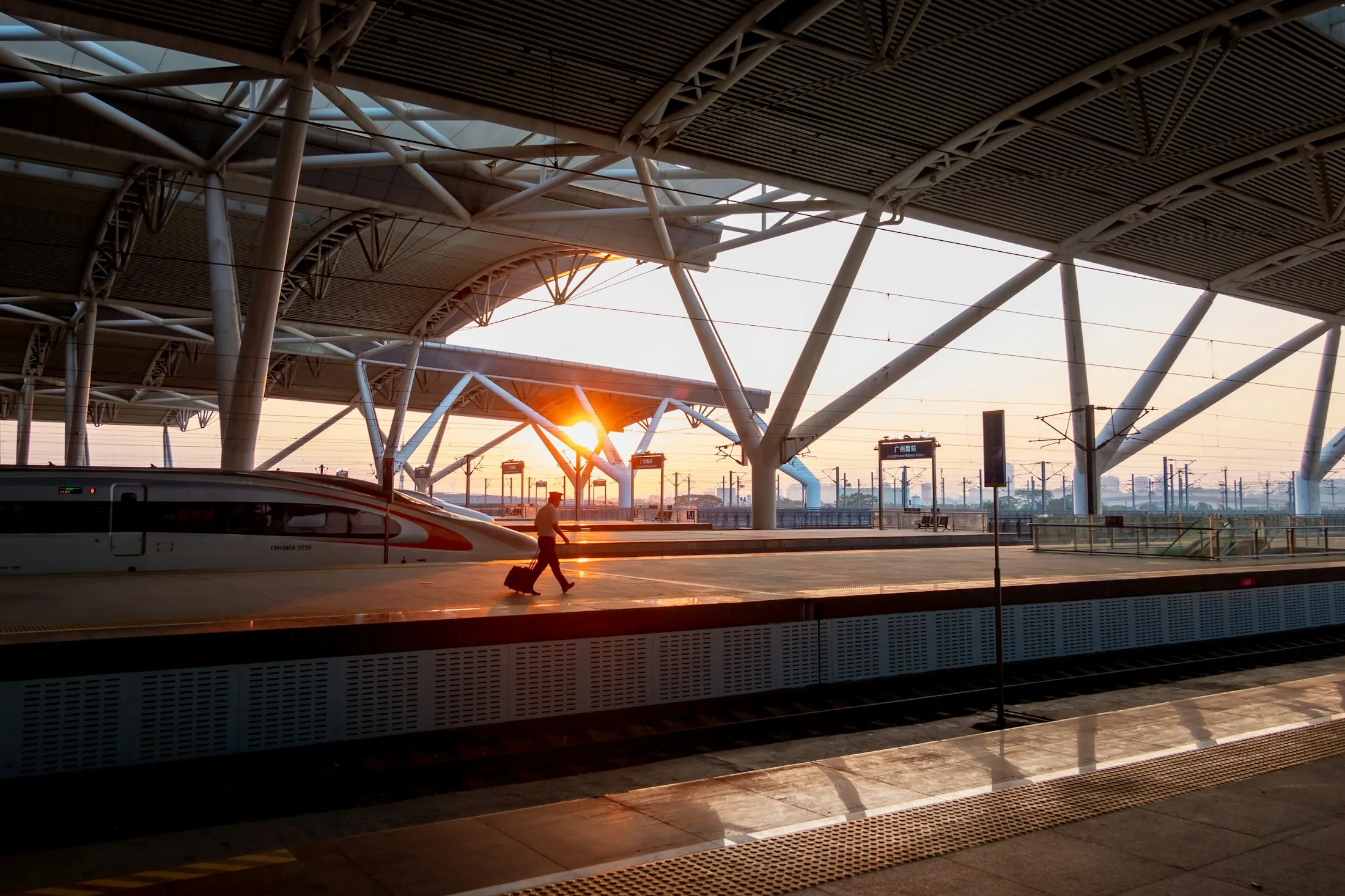 A lone traveller pulling a suitcase along an empty train platform in low golden light
