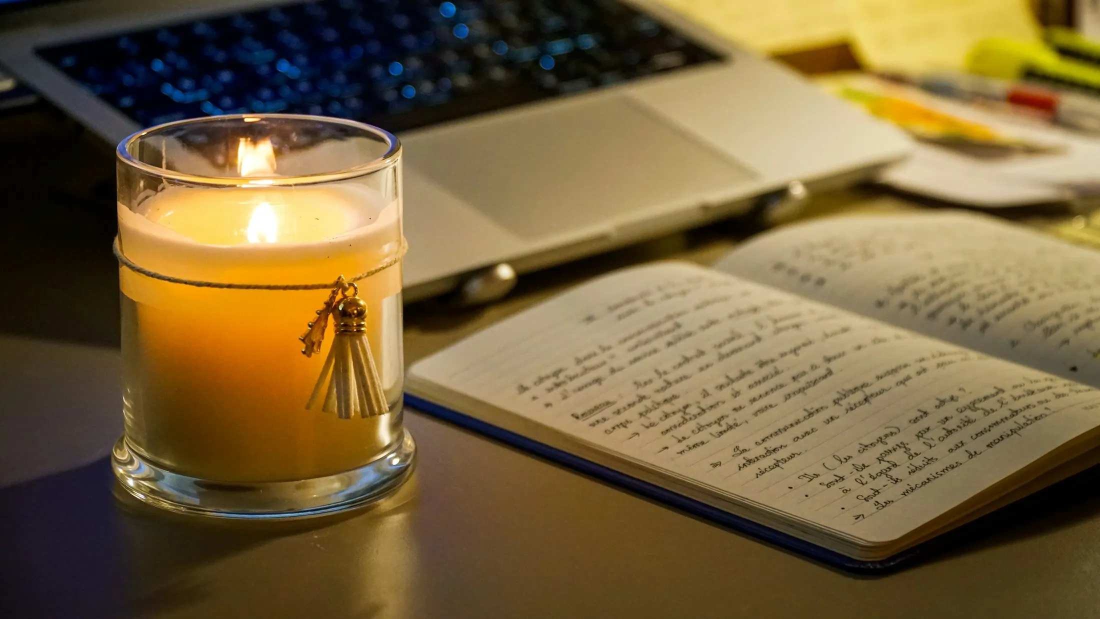 A candle beside an open notebook of handwritten notes on a desk at night
